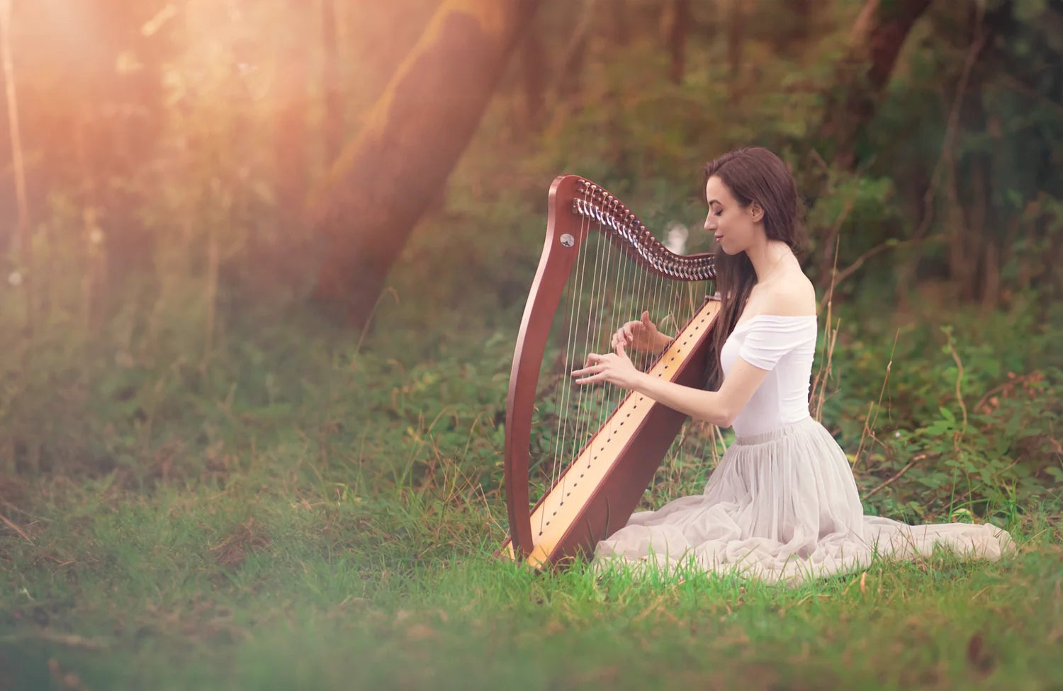 Claire Heffernan playing the harp outdoors on green grass surrounded by trees, wearing an elegant dress.