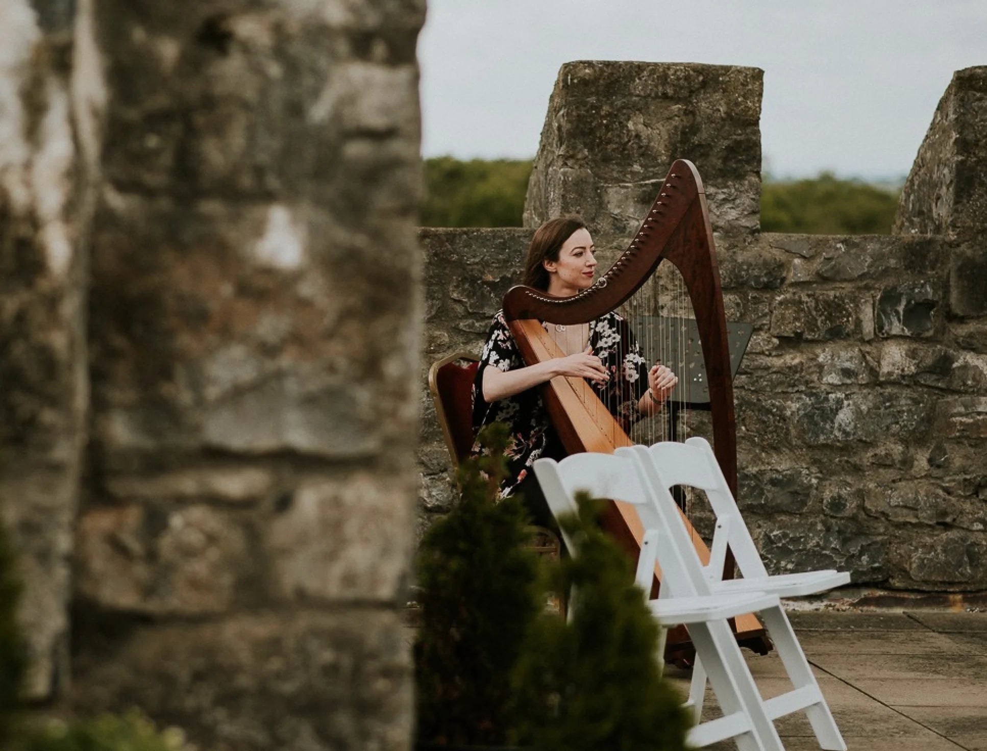 Claire Heffernan playing the harp on top of a castle overlooking the landscape.