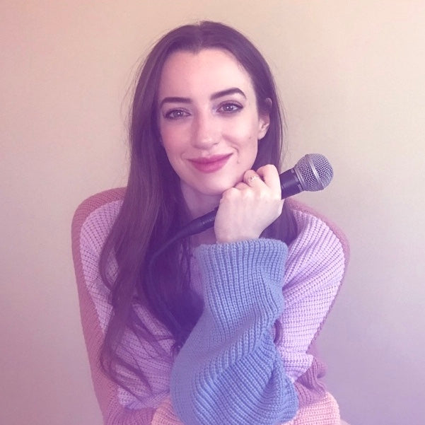 Claire Heffernan wearing a pink and purple jumper, holding a microphone.