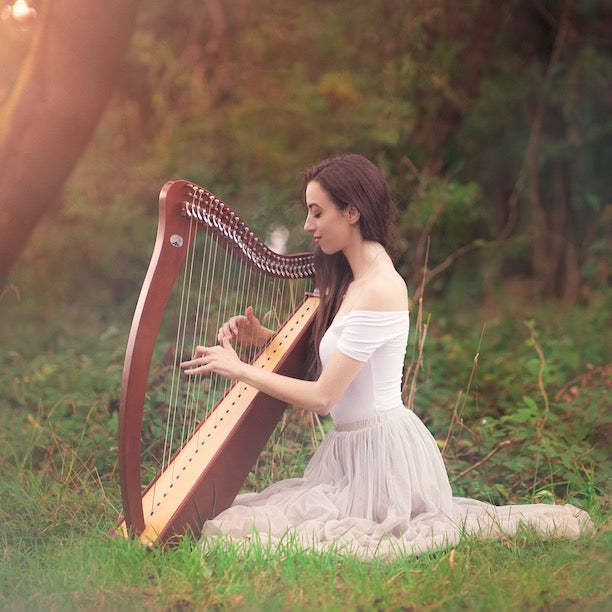 Claire Heffernan playing the harp in a peaceful field surrounded by trees, wearing an elegant dress.
