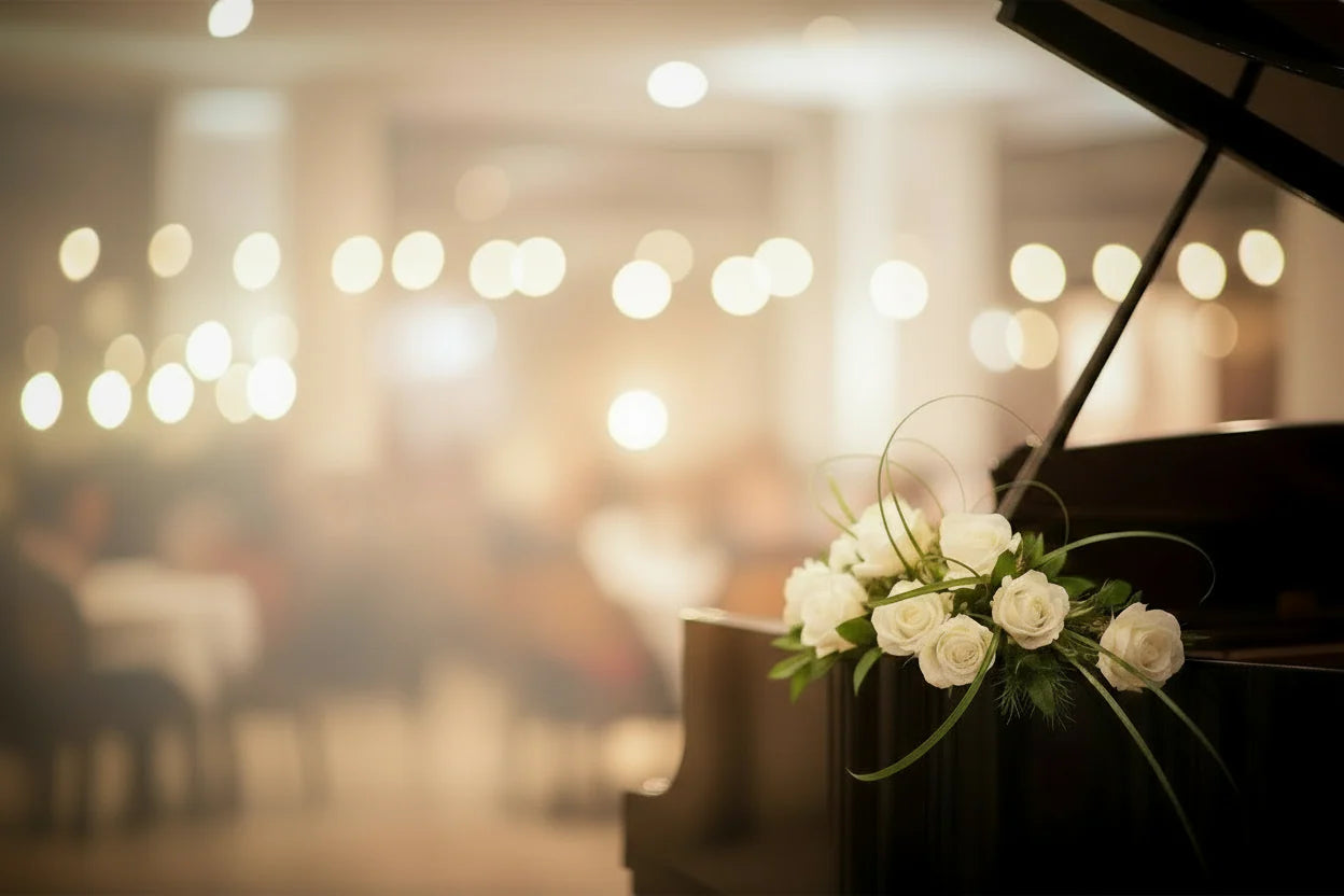 A black grand piano decorated with light flowers, with a softly blurred group of people in the background.