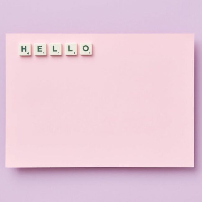 HELLO spelled out with Scrabble tiles on pink card background.