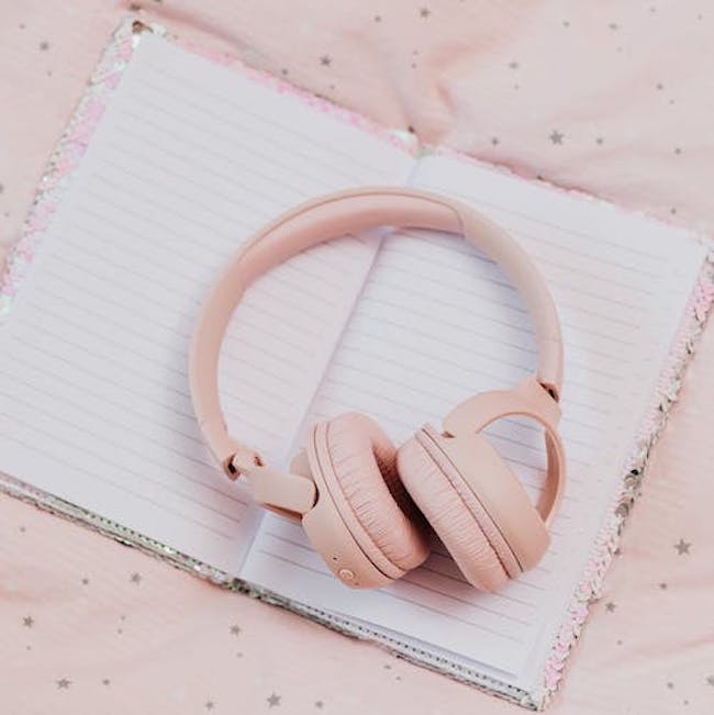 Flat lay of pink headphones resting on a notebook.